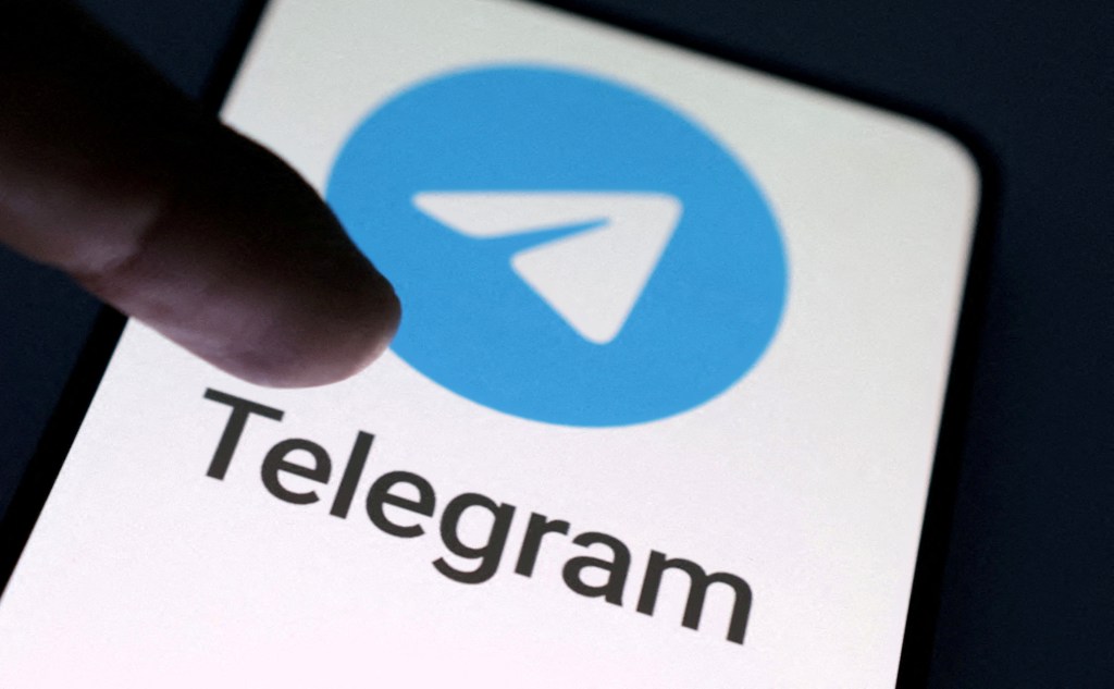 The finger points to the Telegram app logo on the mobile screen